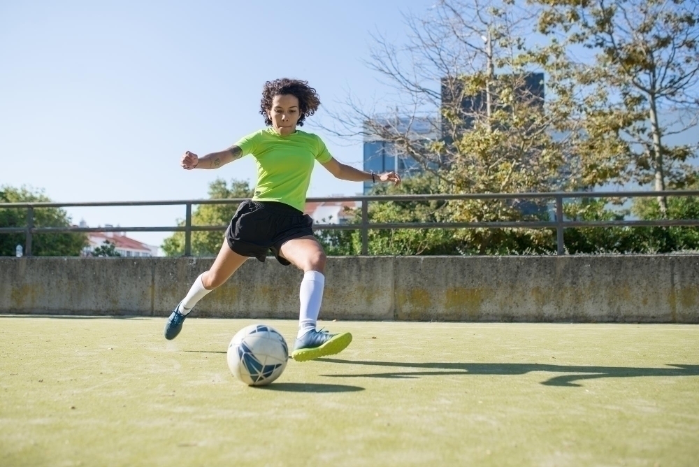 Determined young woman playing football. Sportswoman in bright uniform running on field kicking ball. Sport leisure active lifestyle concept