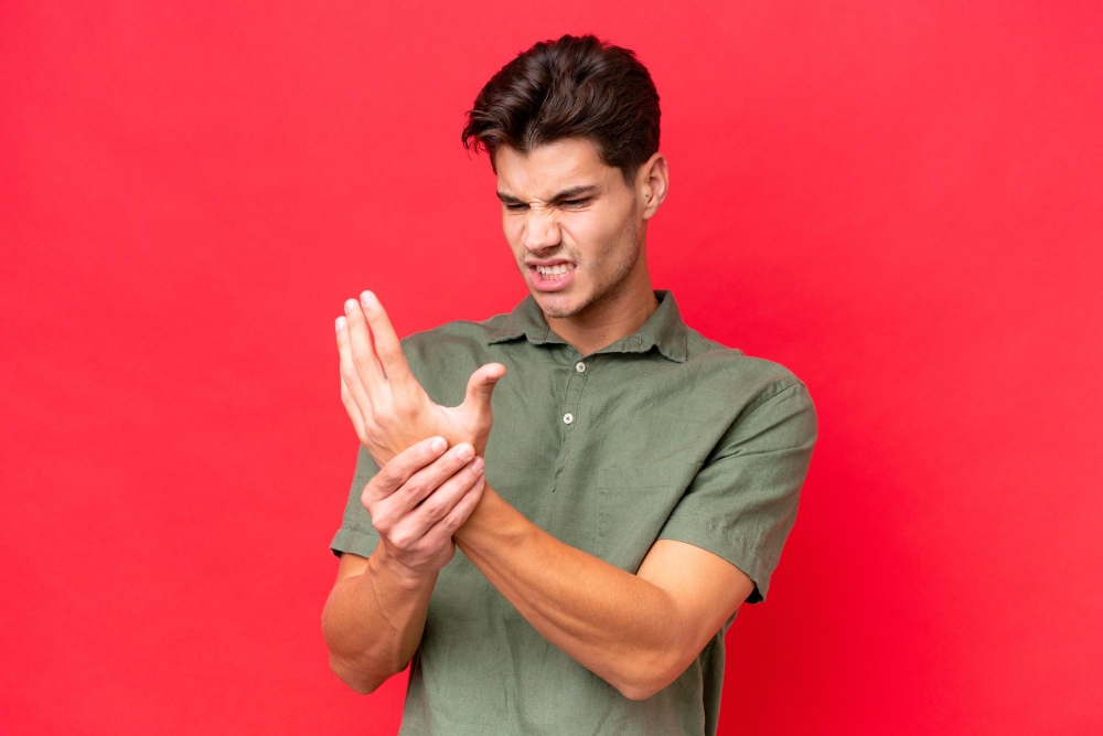 Young caucasian handsome man isolated on red background suffering from pain in hands