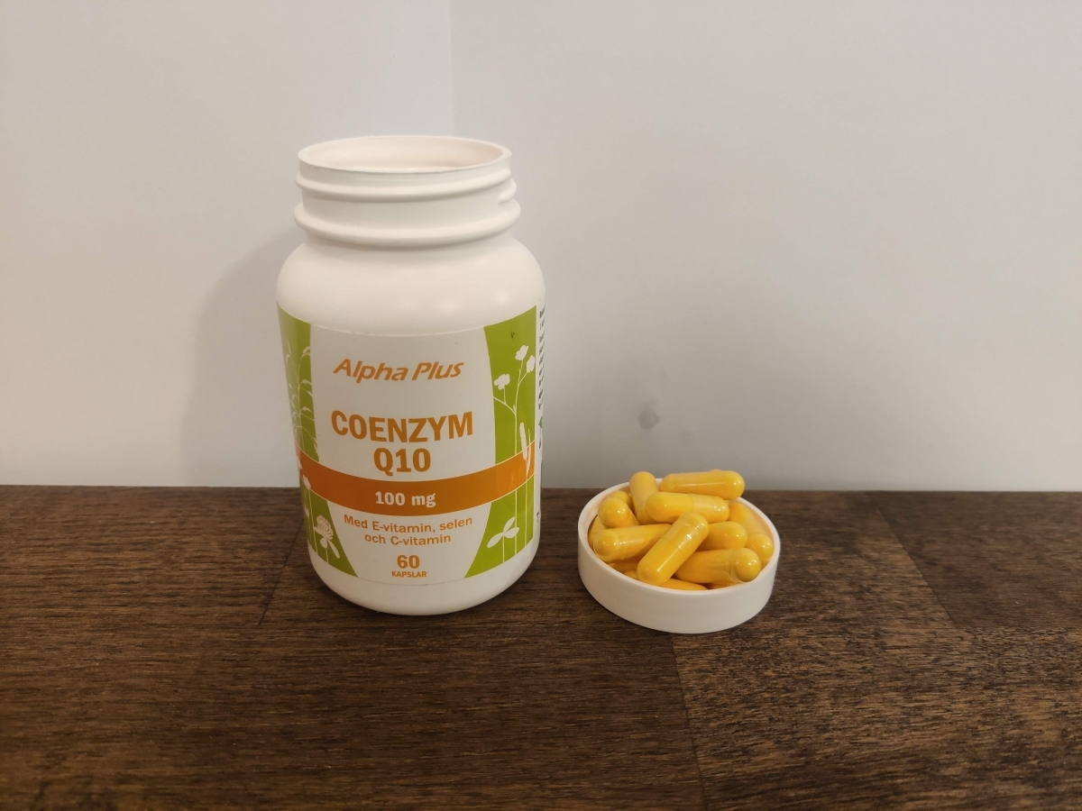 Alpha Plus Coenzym Q10 på träbord med kapslar bredvid, taget av oss
