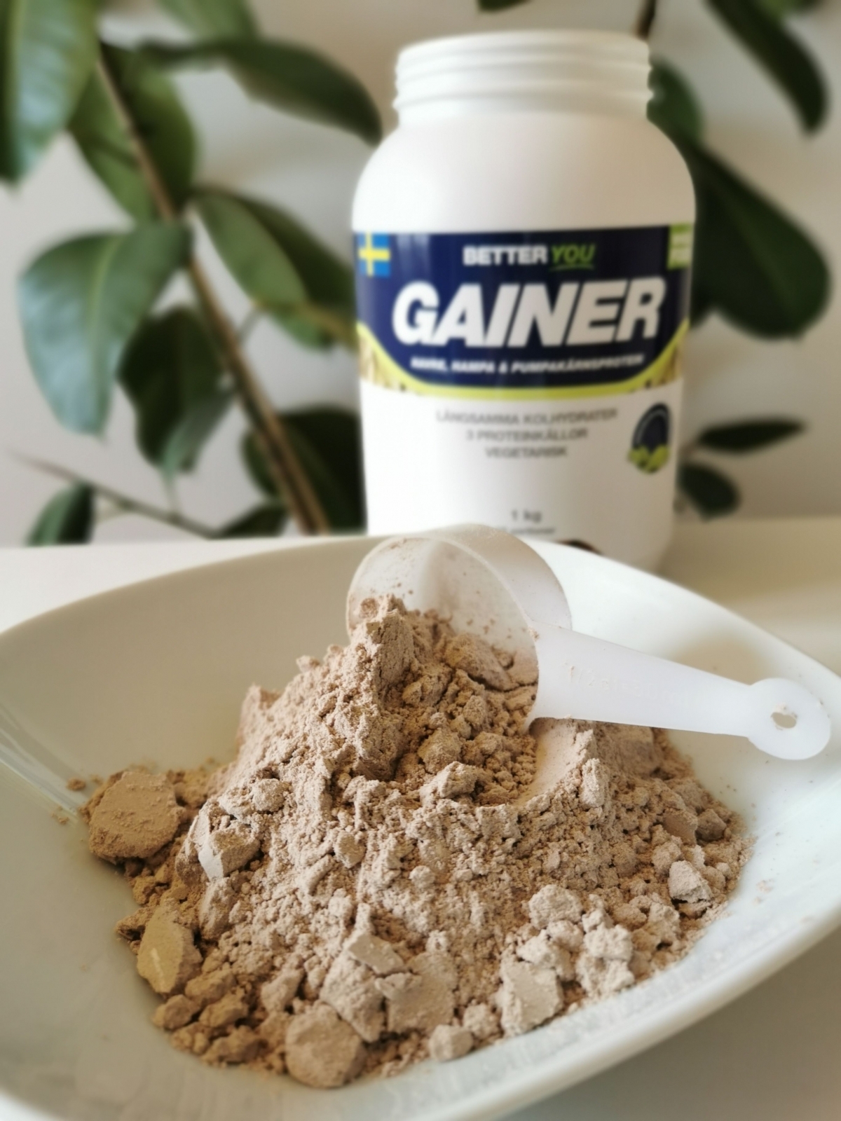 Pulver i skål med skopa framför burken Better You Vegetarisk Gainer fotad i dagsljus