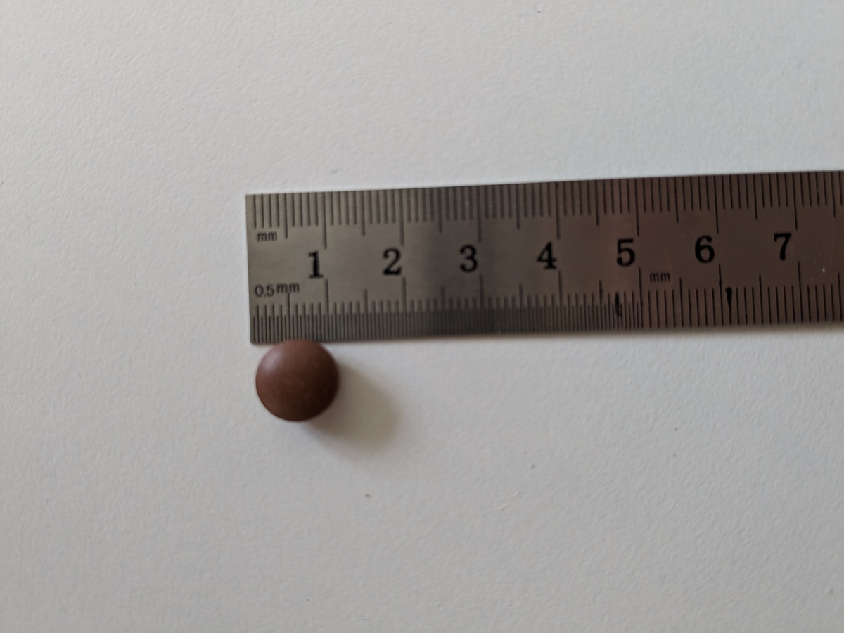 Tablett bredvid linjal som visar cirka 8 mm i diameter, fotograferad av oss