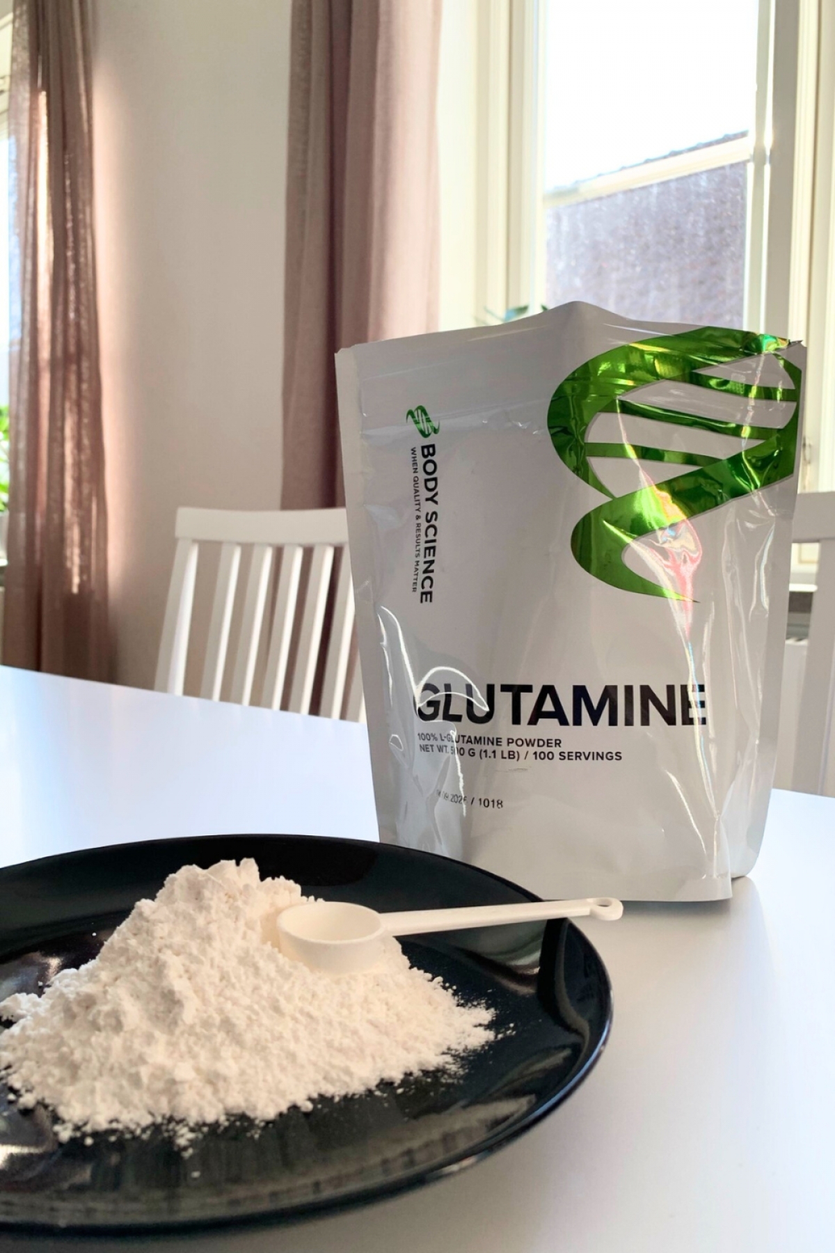 Glutaminpulver på tallrik med egen skopa och förpackningen i bakgrunden, vårt foto