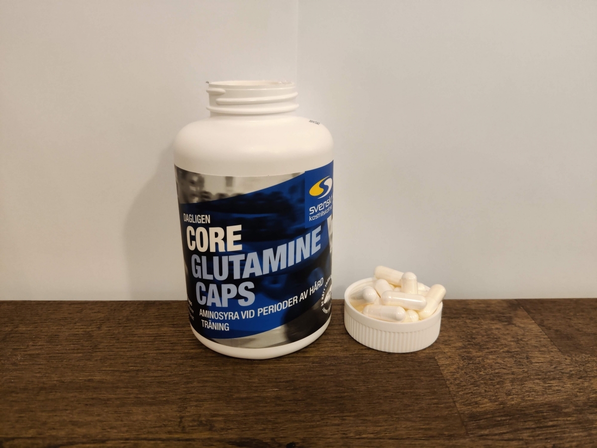 Core Glutamine Caps med kapslar bredvid locket i varm inomhusbelysning