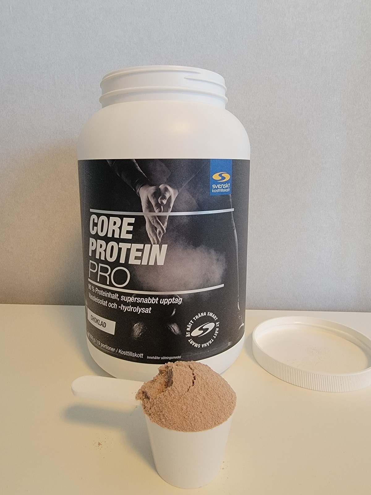 Core Protein Pro choklad med öppet lock och fylld skopa, fotad av oss under testet