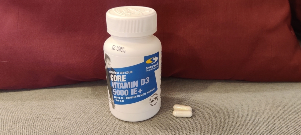 Core Vitamin D3 med två kapslar bredvid på tyg, tagen i vardagsrummet