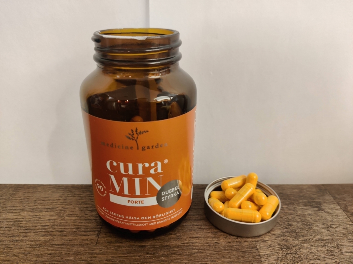 Närbild på MedicineGarden CuraMIN-burk och upphällna kapslar, tagen av oss