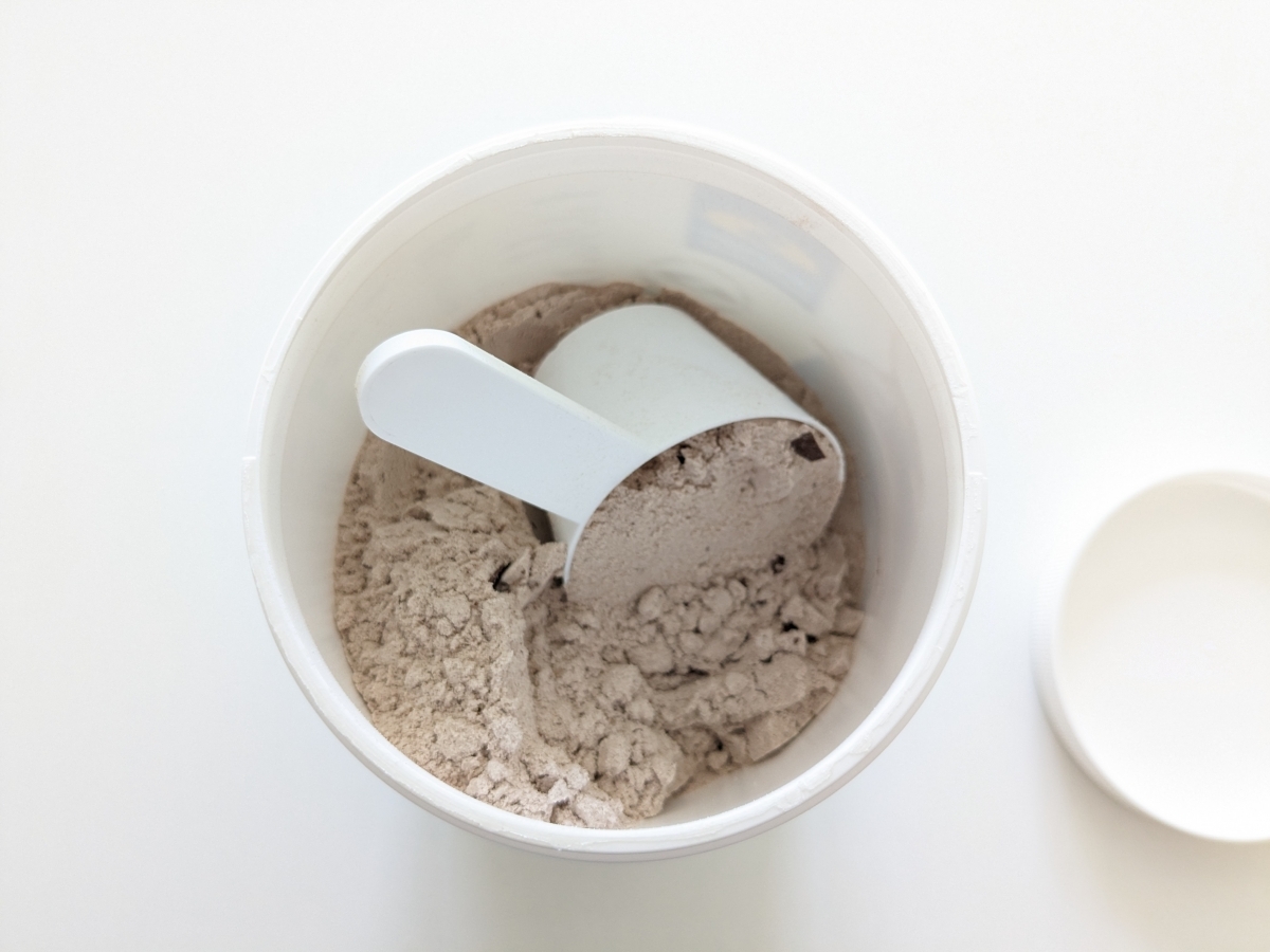 Öppen burk med Diet Shake choklad och skopa, chokladbitar syns i pulvret, fotad av oss under testet