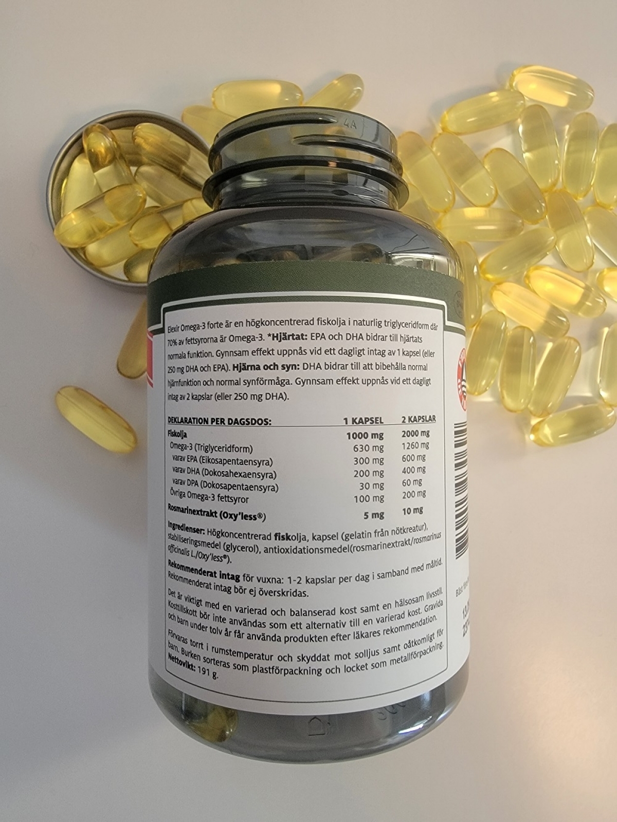 Baksida med doseringstext och kapslar runt burken för Elexir Omega-3 Forte, taget av oss
