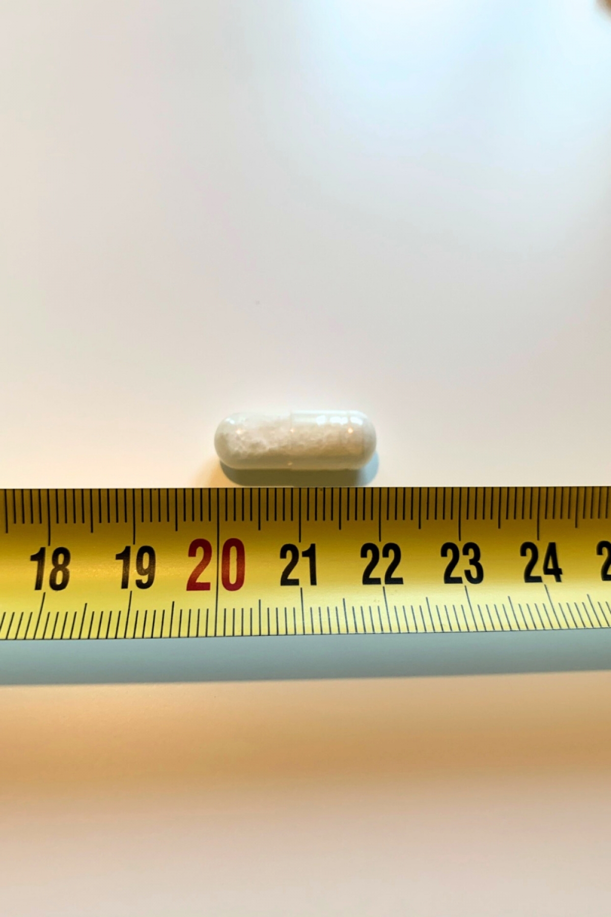 En kapsel L-Lysin bredvid måttband cirka två centimeter vårt eget storlekstest