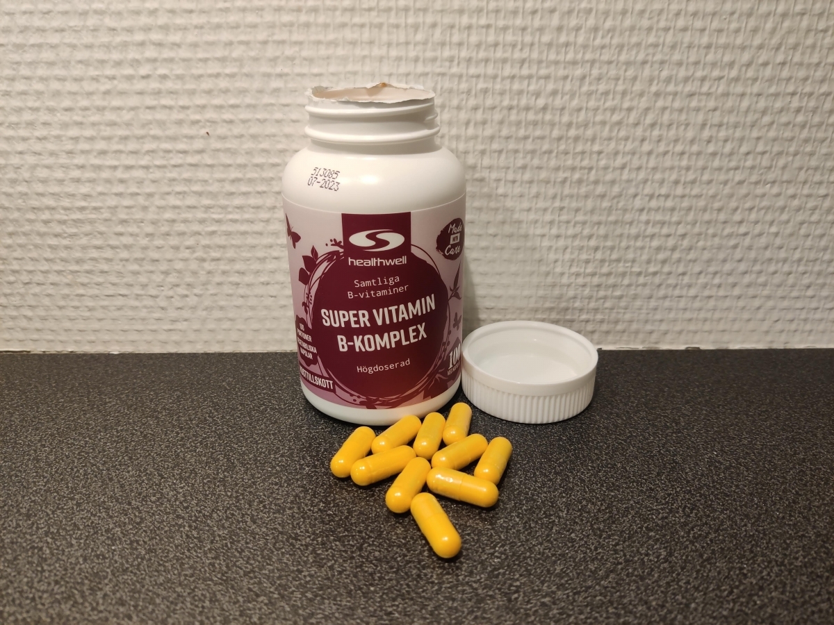 Healthwell Super Vitamin B-komplex fotograferad av oss under testet, öppnad burk med gula kapslar på bänkskiva