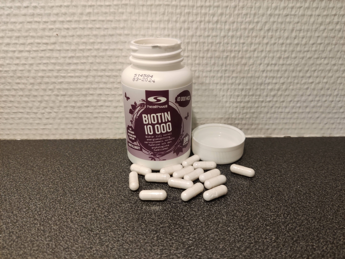 Healthwell Biotin 10 000 kapslar fotade av oss på mörk bänkskiva med öppnad burk