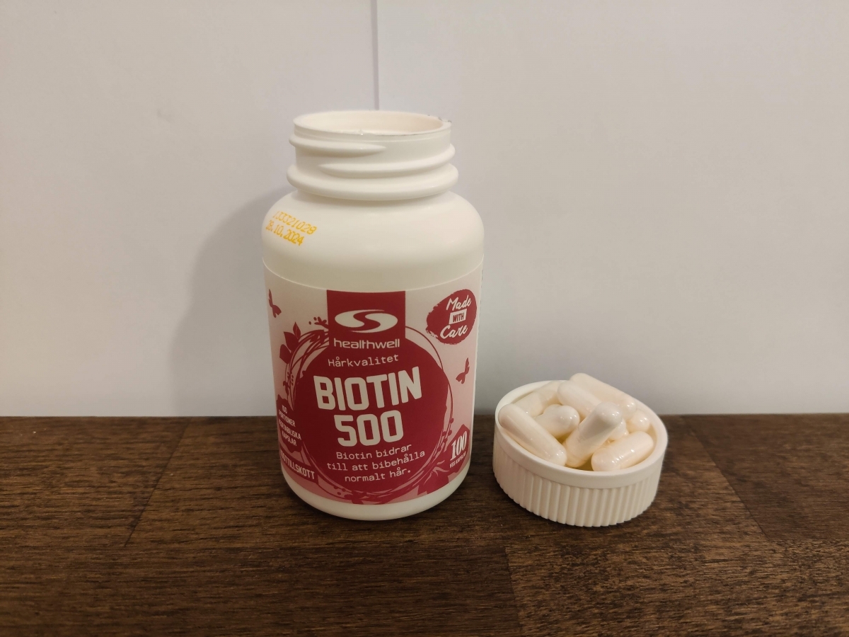 Healthwell Biotin 500 framifrån med kapslar intill, eget foto