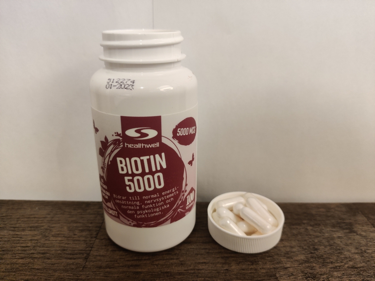 Healthwell Biotin 5000 på träbord med kapslar nära foto av oss