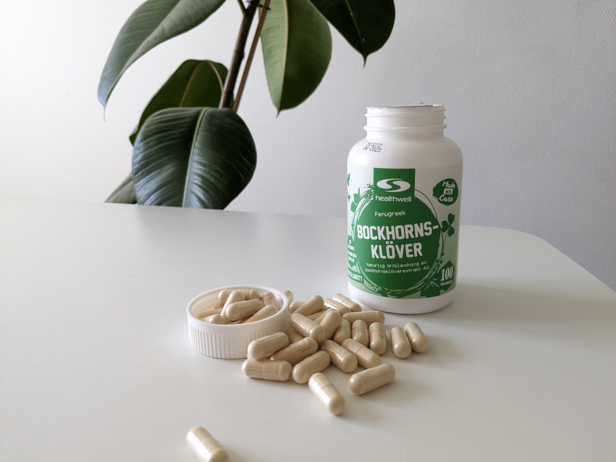 Vår egen bild av Healthwell Bockhornsklöver, burk och kapslar på bordet med grön växt i bakgrunden under testet