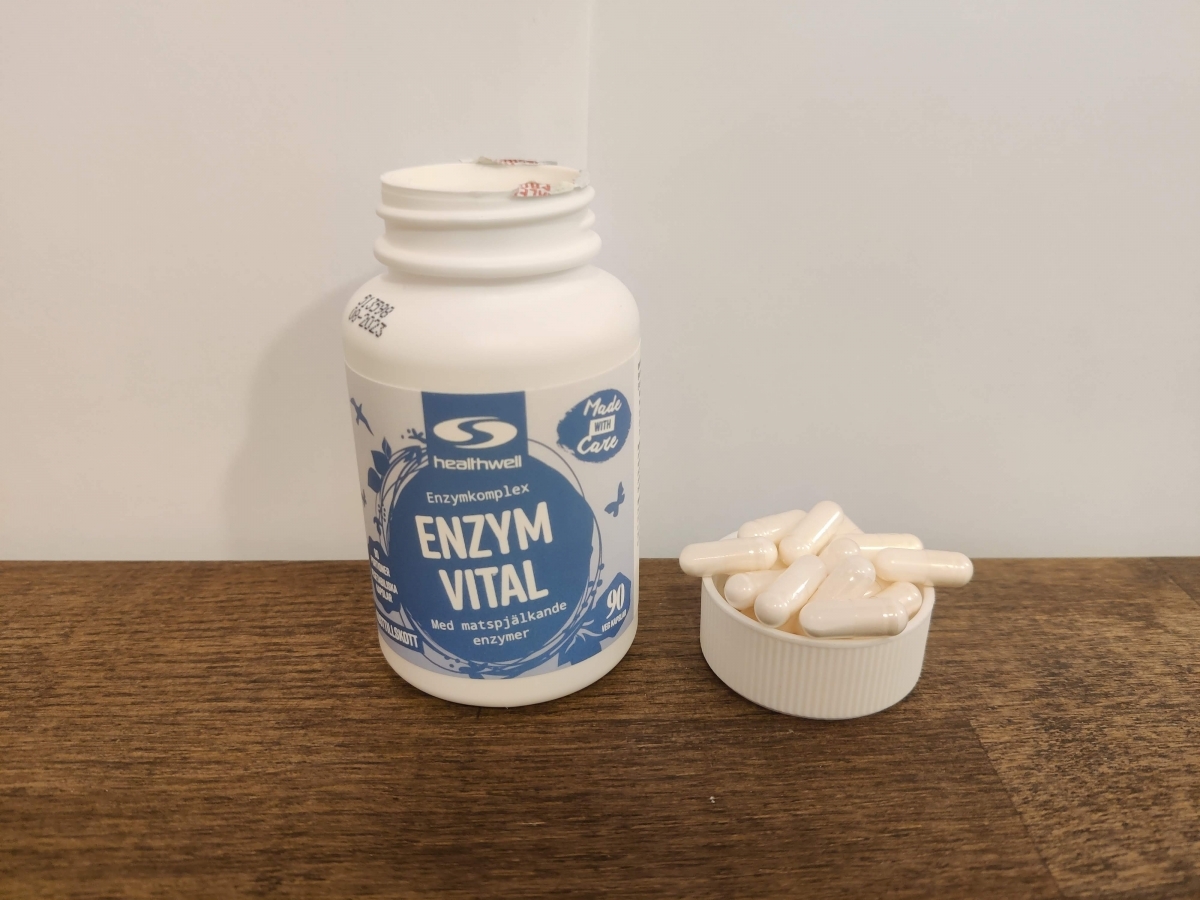 Healthwell Enzym Balans på träbord med kapslar bredvid, taget under test