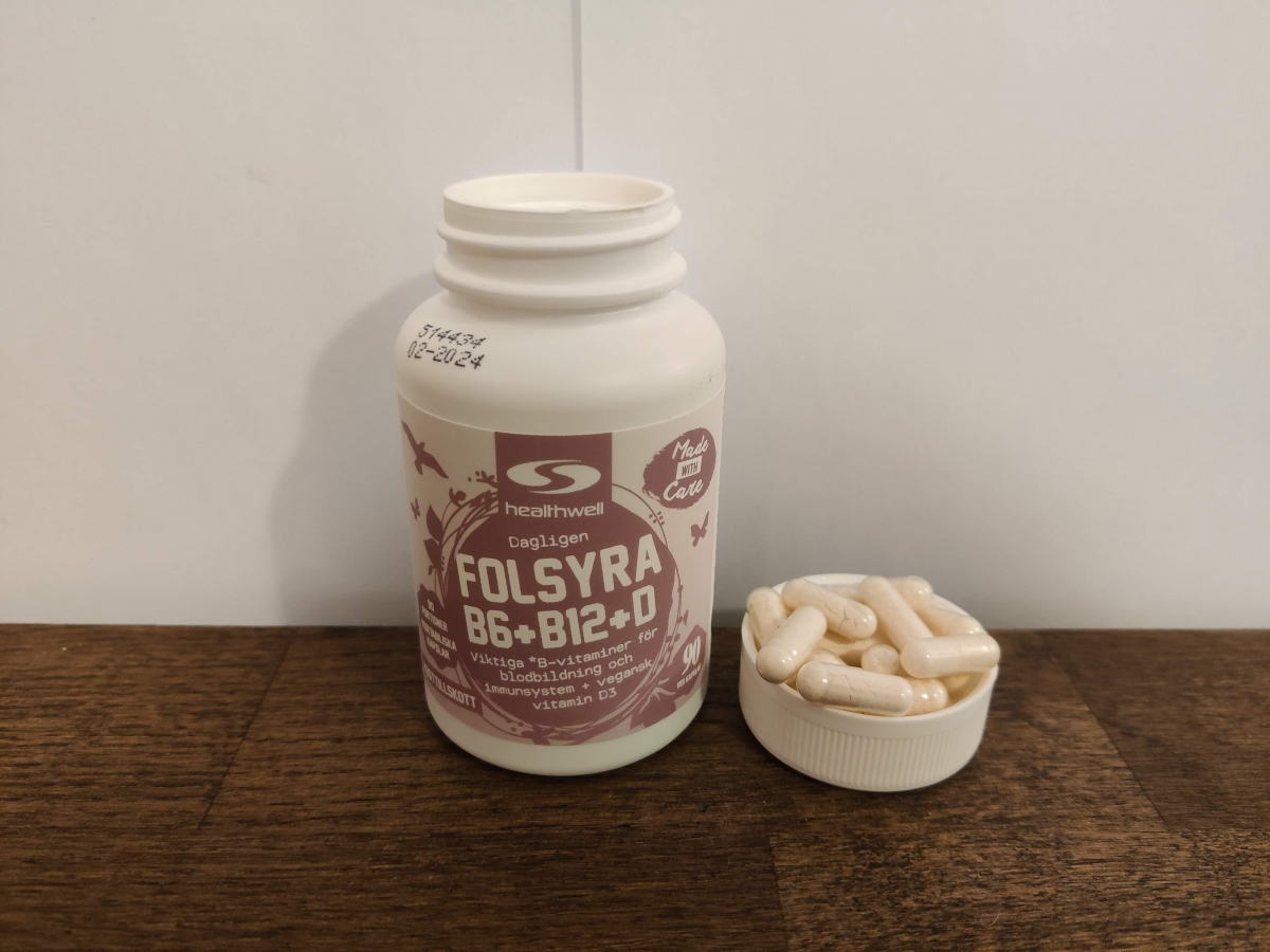 Healthwell Folsyra B6 B12 D på träbord bredvid kapslar, vårt eget foto