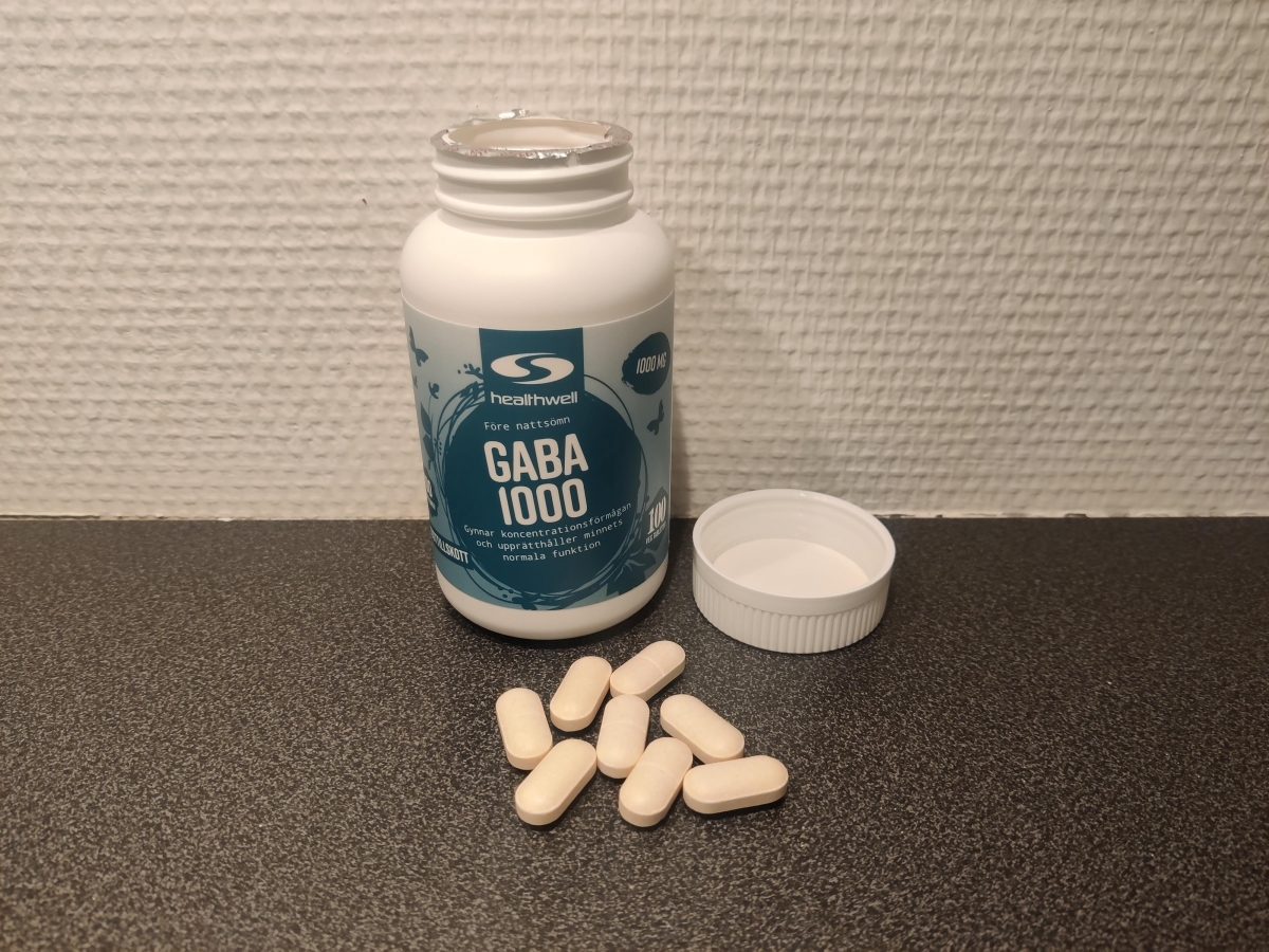 Öppen burk Healthwell GABA 1000 med tabletter framför, fotad av oss