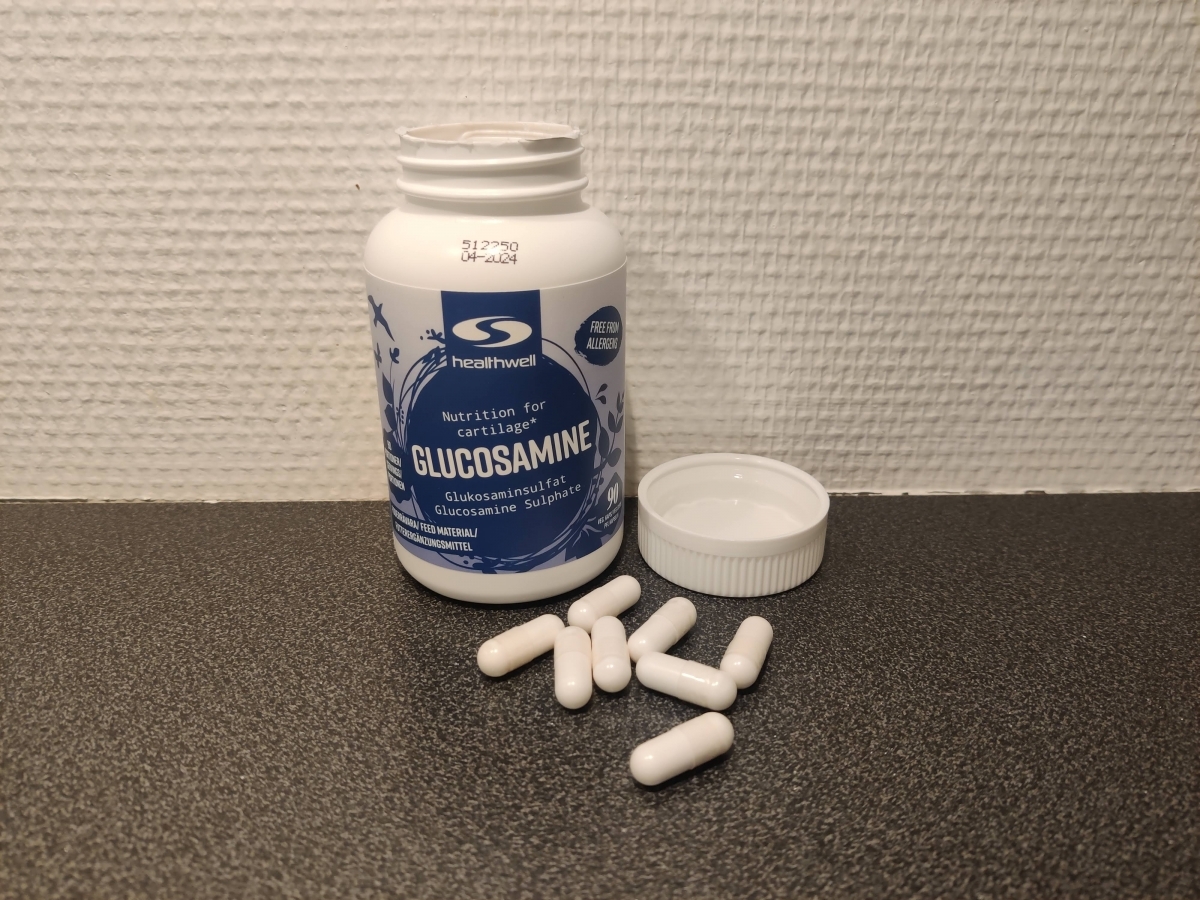 Healthwell Glukosamine burk och kapslar på bänkskiva fotad av oss under testet
