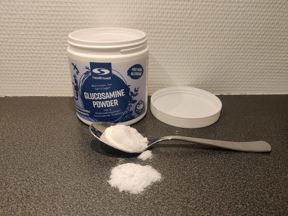 Öppen burk Healthwell Glucosamine Powder med sked pulver på bänken, foto taget av oss under testet