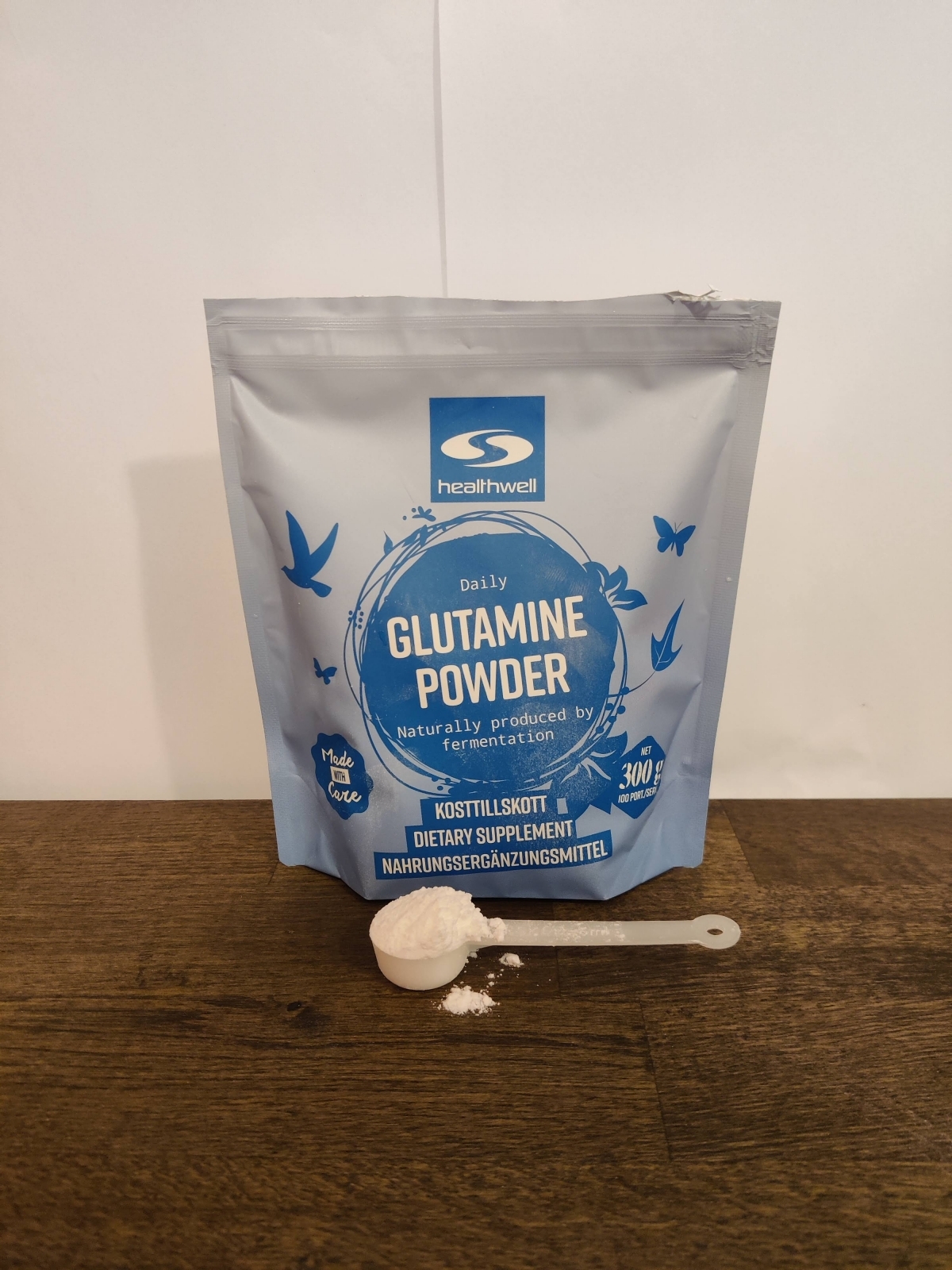 Healthwell Glutamine Powder med uppmätt skopa på trä, under vår testperiod