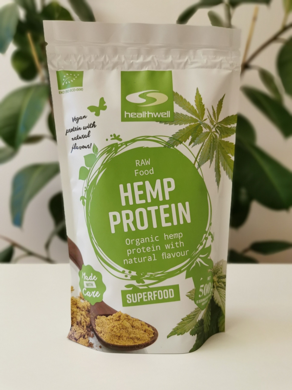 Healthwell Hampaprotein EKO på ljus bänk med grön växt i bakgrunden, fotad av oss