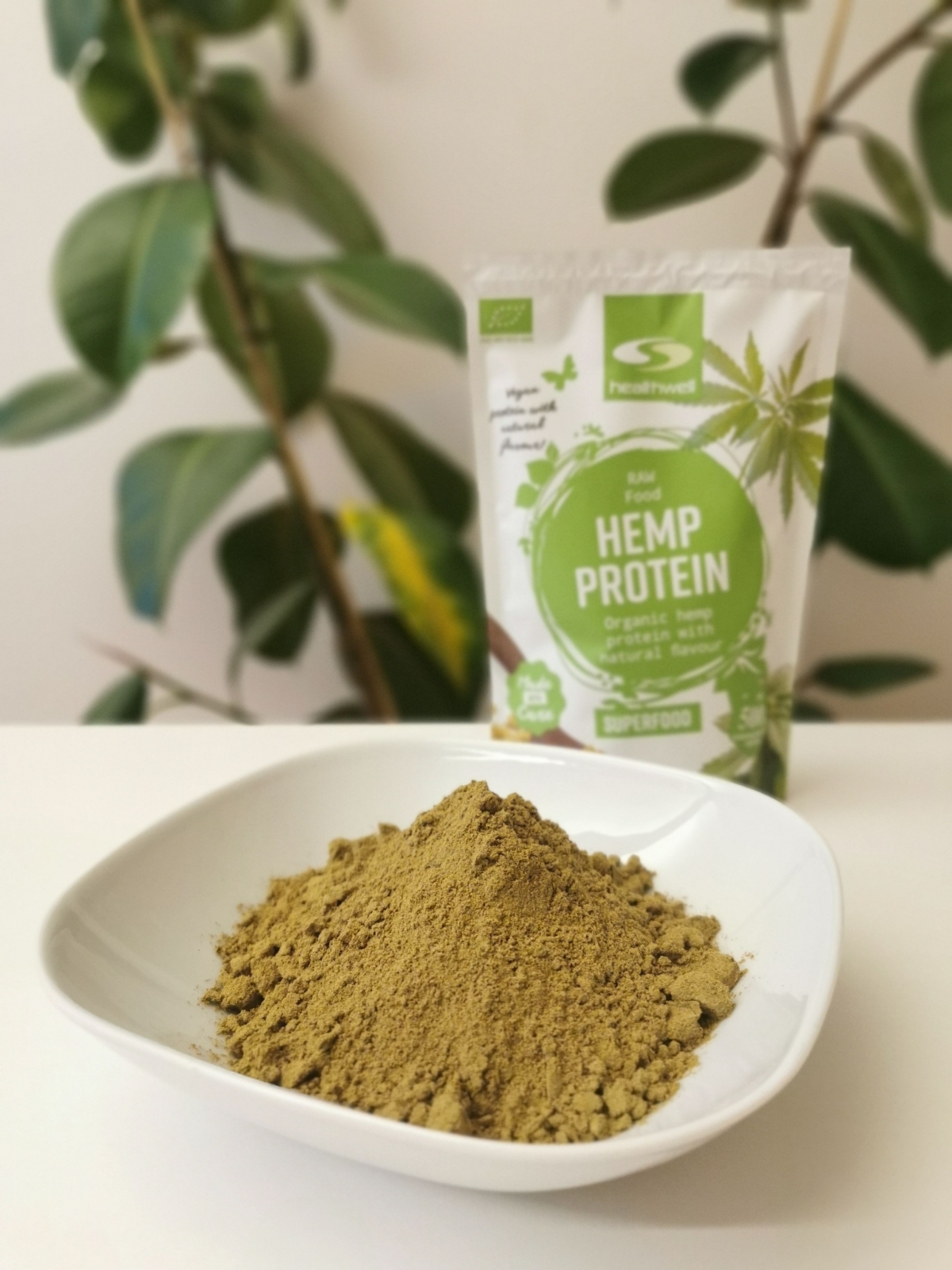 Hampaproteinpulver i vit skål med förpackningen suddad bakom, fotad av oss