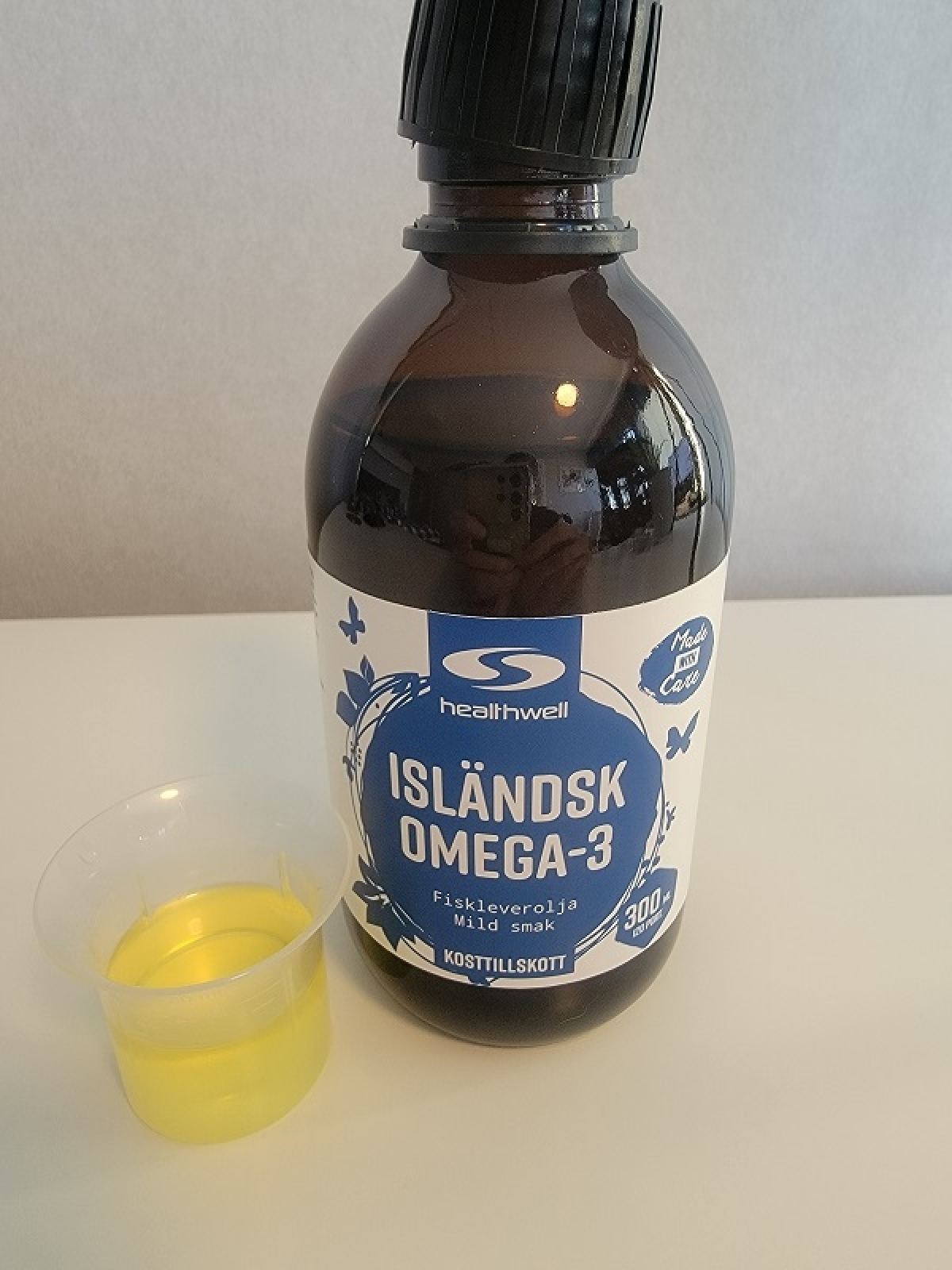 Healthwell Isländsk Omega-3 fotograferad av oss under testet, flaska med provkopp och ljusgul olja