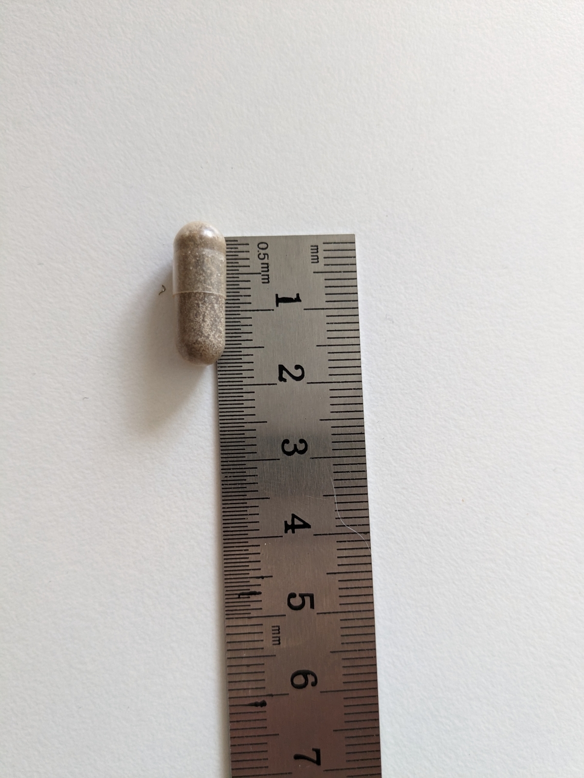 Kapsel från Healthwell Järn Skonsam bredvid linjal, ungefär 1,8 cm
