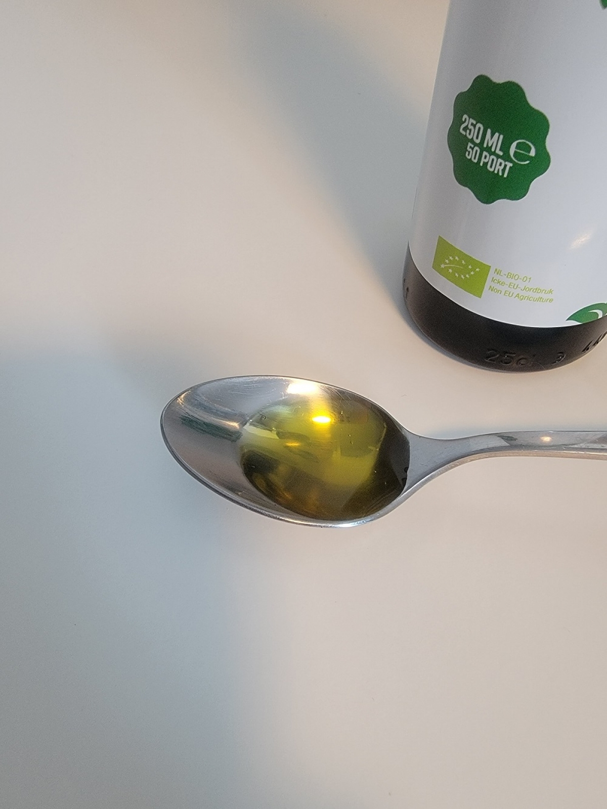 Tesked med klar, gyllene linfröolja från Healthwell framför flaskans etikett, foto av oss