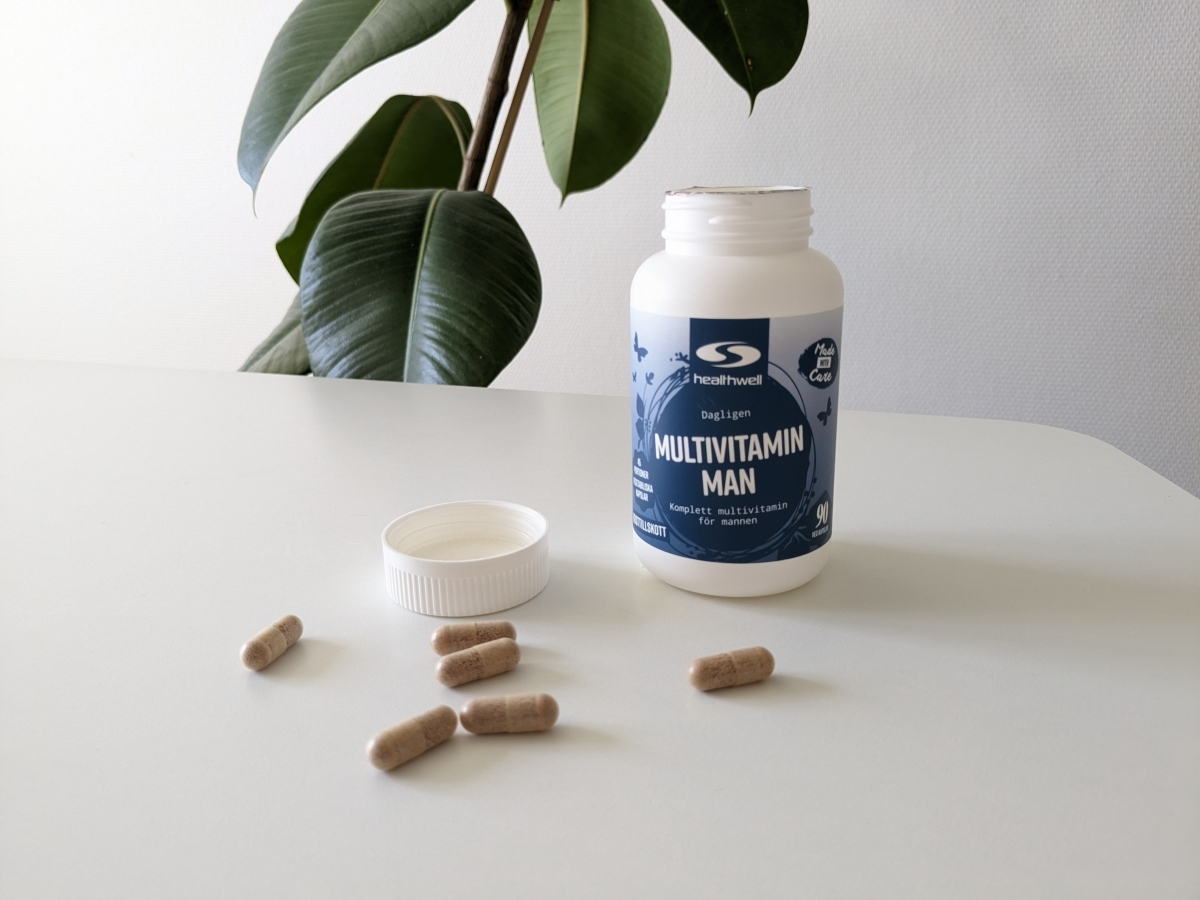 Healthwell Multivitamin Man fotograferad av oss under testet – öppen burk med kapslar på bord i naturligt ljus