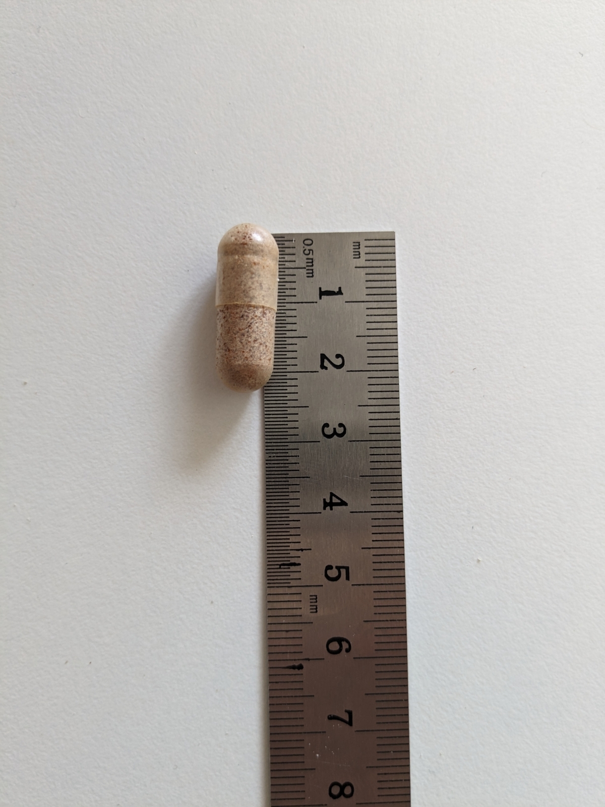 Kapsel från Healthwell Multivitamin Man bredvid linjal, cirka 2 cm lång