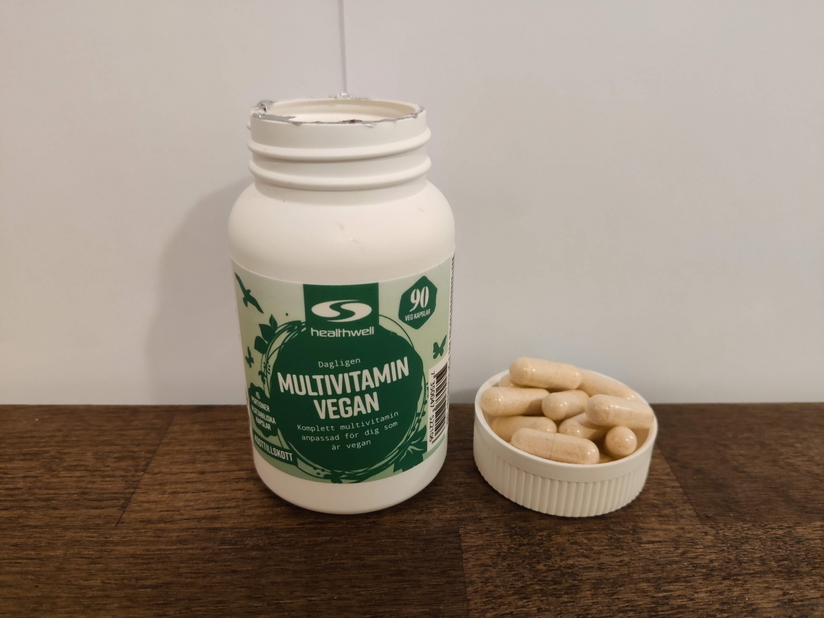 Närbild tagen av oss på Healthwell Multivitamin Vegan med kapslar i locket på ett träbord