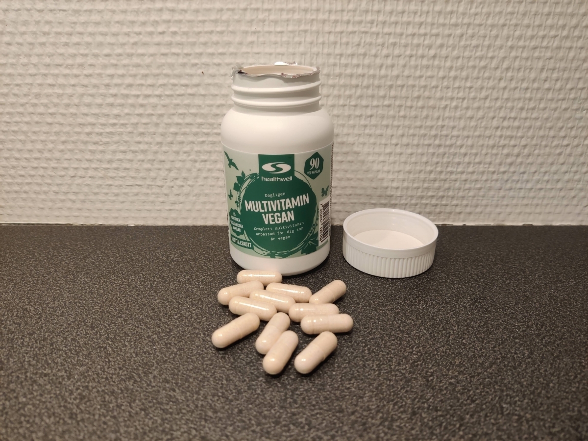 Healthwell Multivitamin Vegan fotograferad av oss – öppnad burk med ljusgula kapslar på bänken
