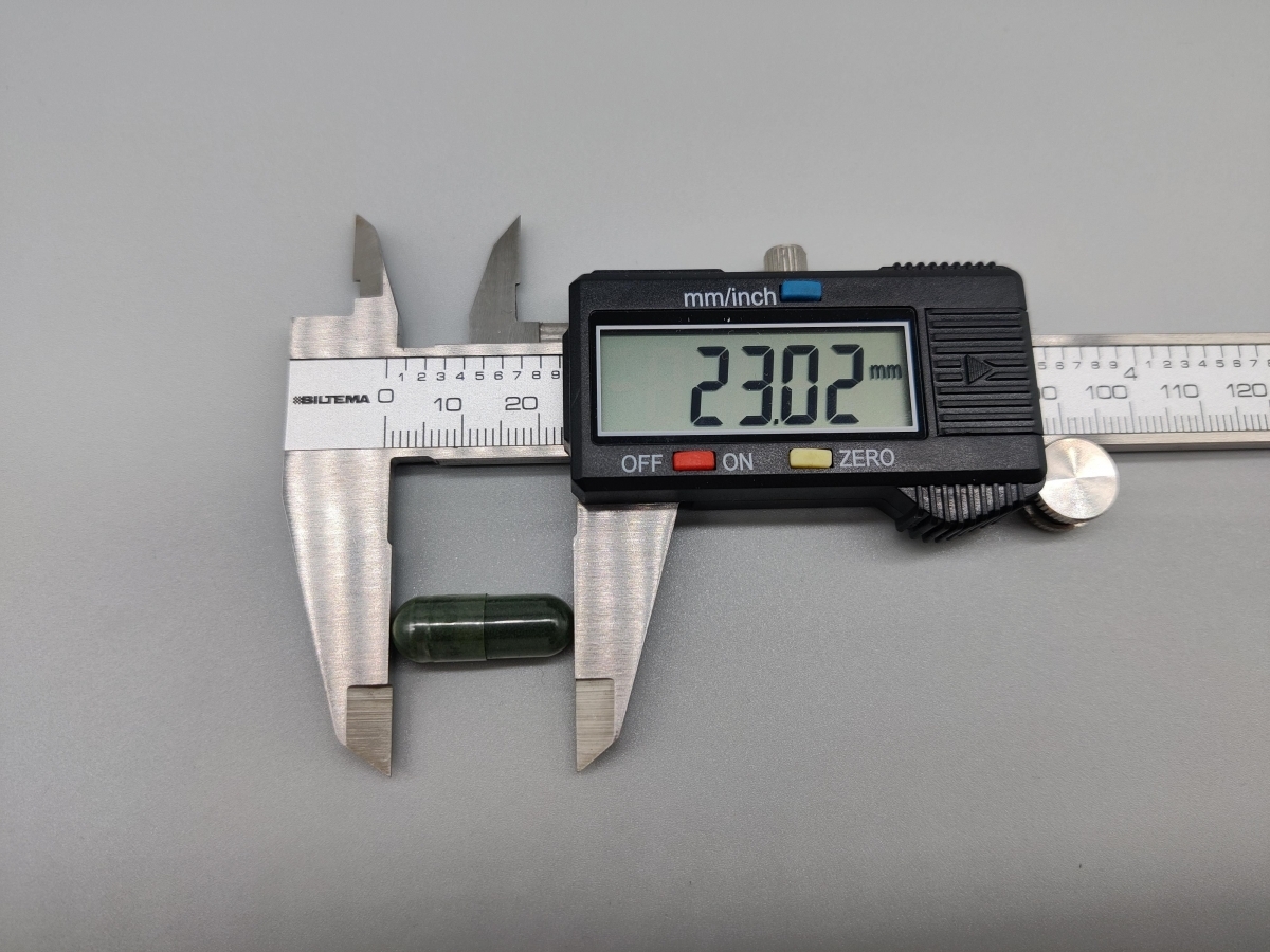 Skjutmått som visar kapselns längd runt 23 mm, dokumenterat av oss