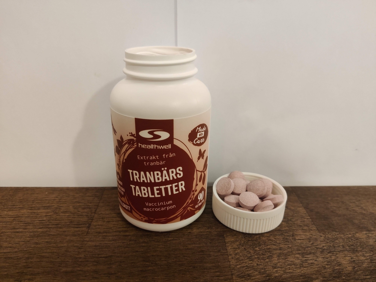 Healthwell Tranbärsextrakt med tabletter intill på träbord, tagen av oss