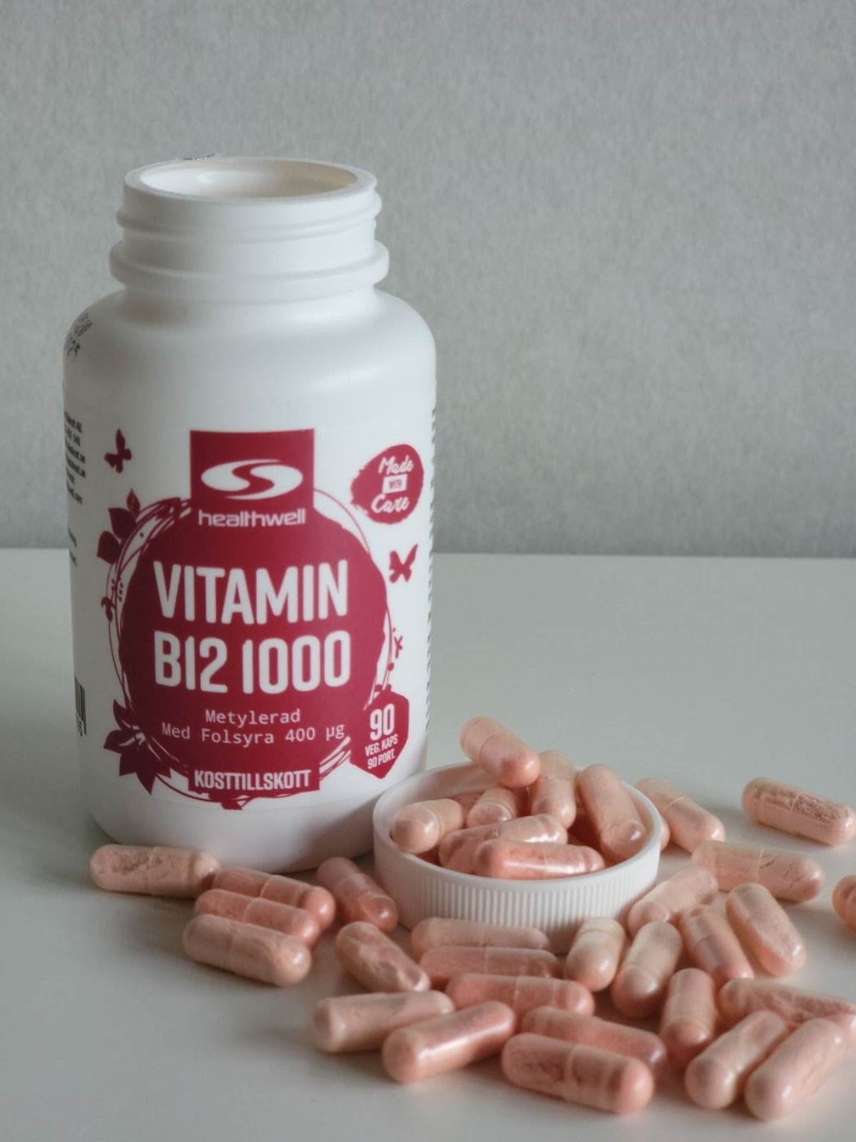 Egen bild av Healthwell Vitamin B12 1000, öppnad burk med rosatonade vegokapslar på bordet under vårt test