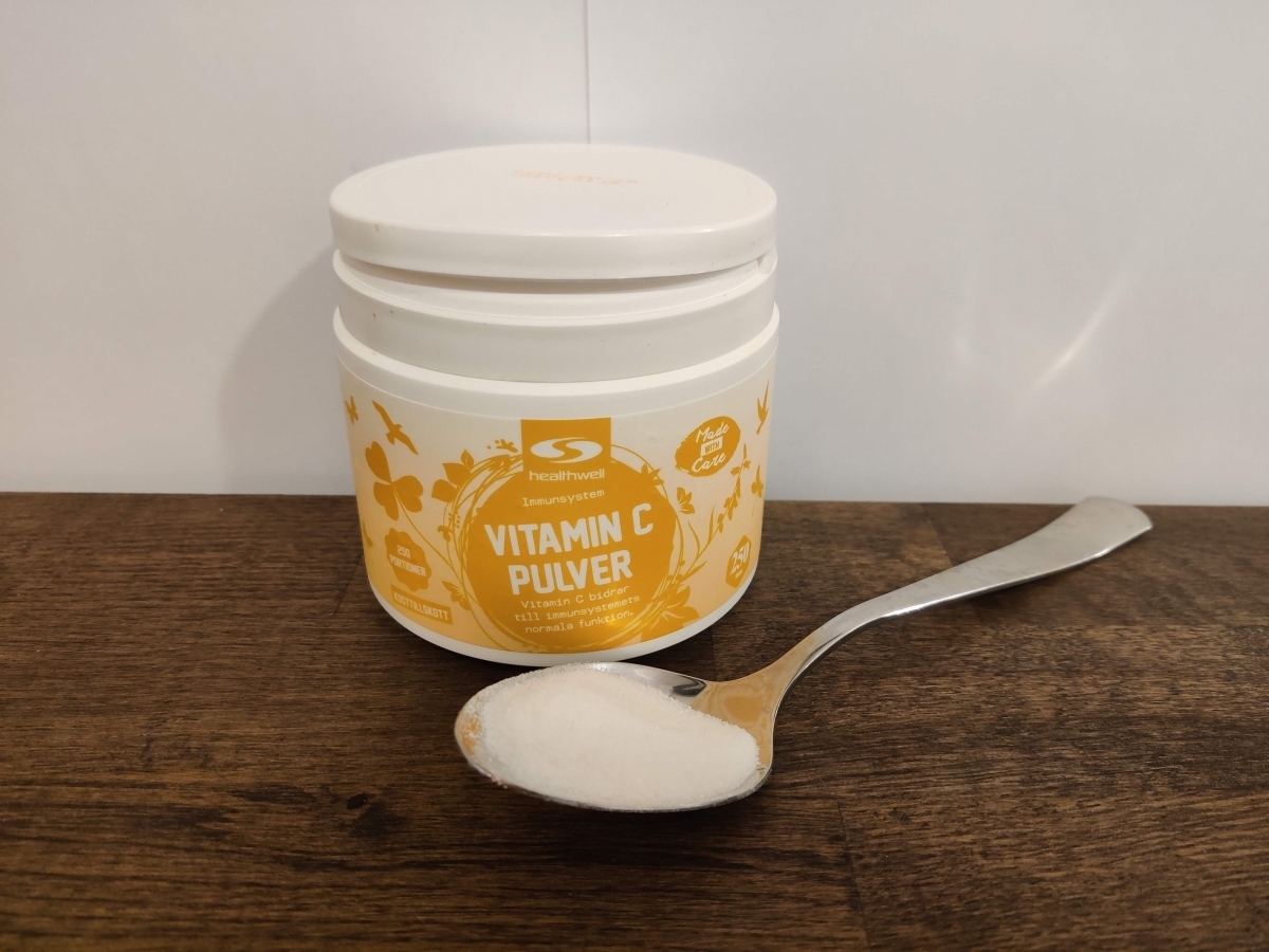 Närbild på Healthwell Vitamin C Pulver på sked framför burken, fotad av oss