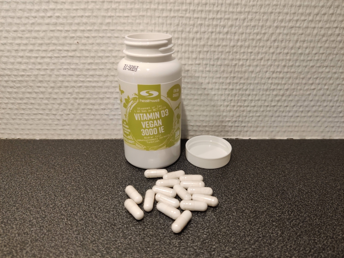 Healthwell Vitamin D3 Vegan 3000 IE med öppnad burk och utspridda kapslar på bänkskiva, foto taget av oss under användning