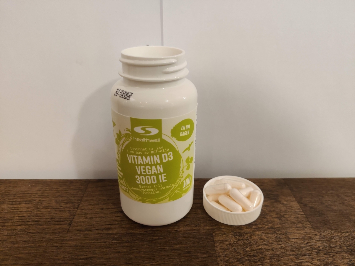Healthwell Vitamin D3 Vegan på träbord med några kapslar bredvid, egen bild i naturligt ljus