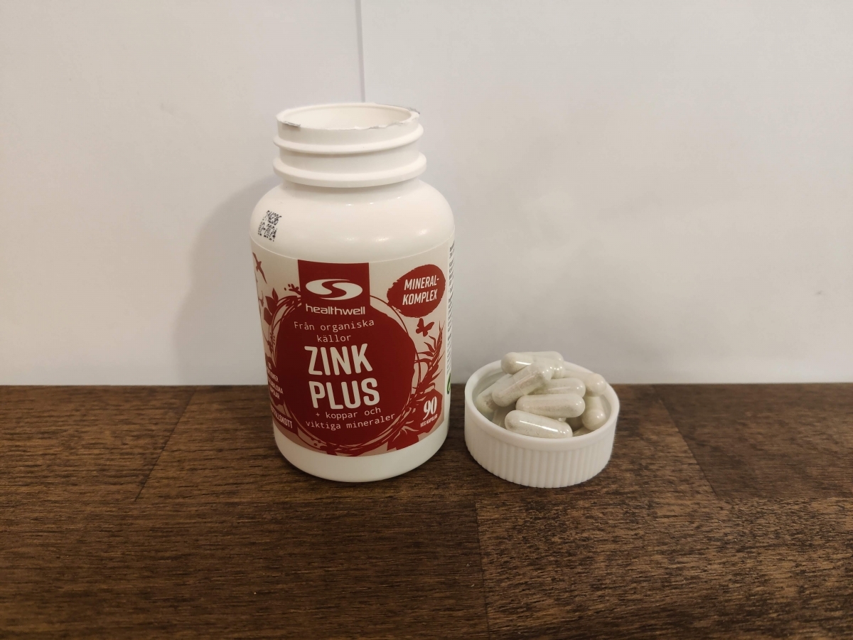 Närbild av Healthwell Zink 25 Plus på träbord med några kapslar i locket, tagen av oss