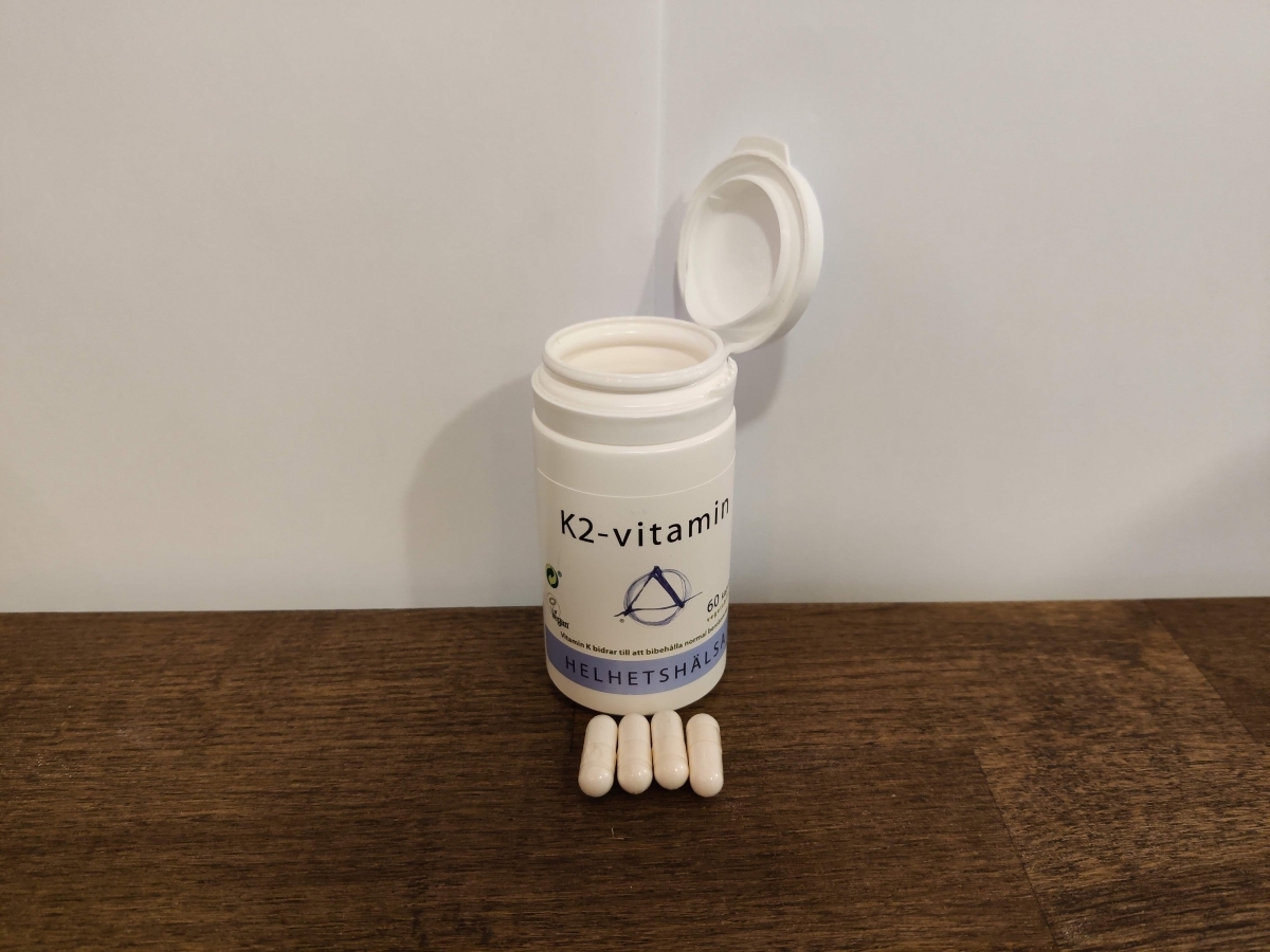 Helhetshälsa K2-Vitamin på träbord med fyra upplagda kapslar, fotograferad i hemmaljus