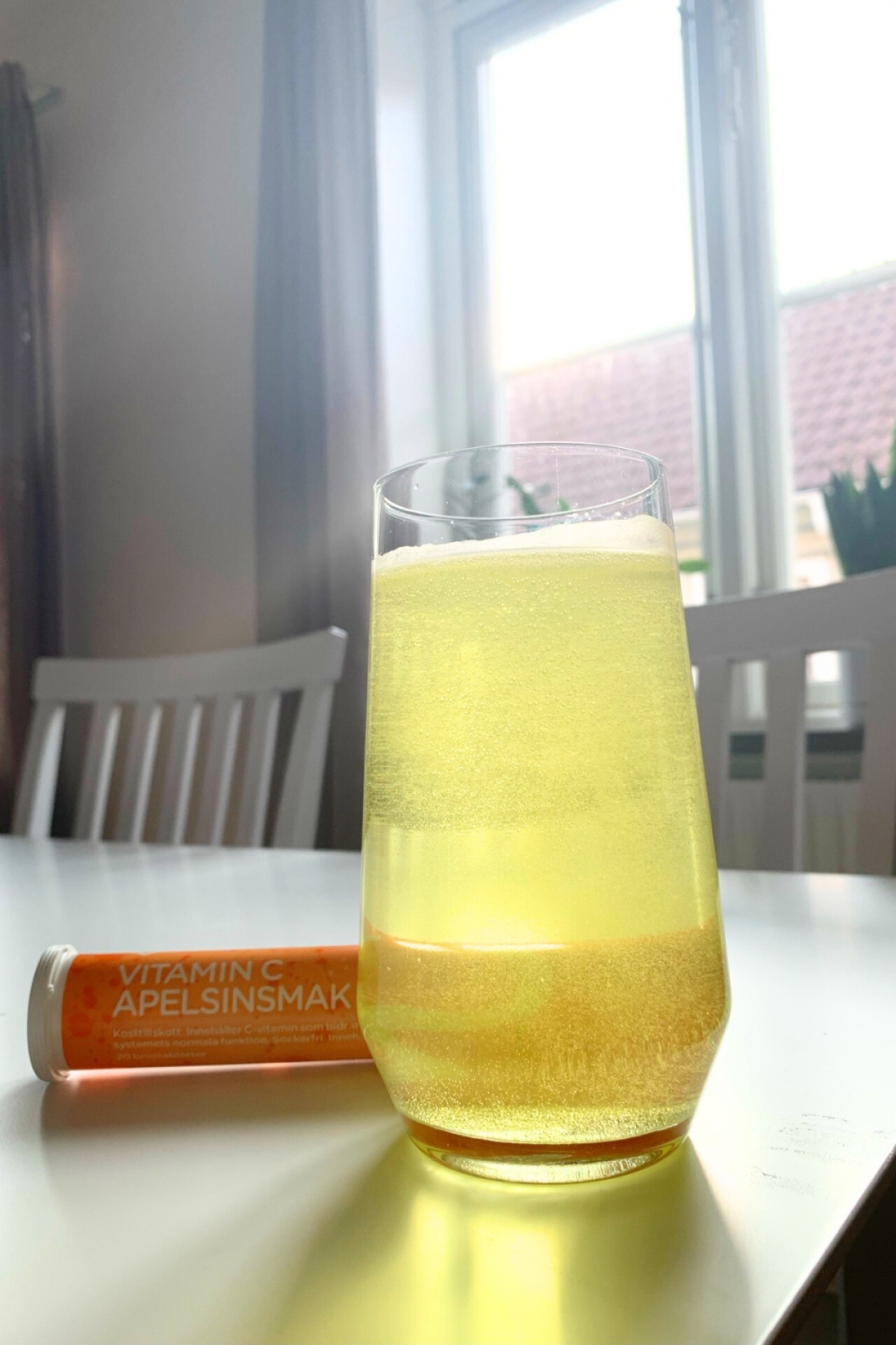 Pärlande glas C-vitamin i morgonljus med rör i bakgrunden, taget av oss