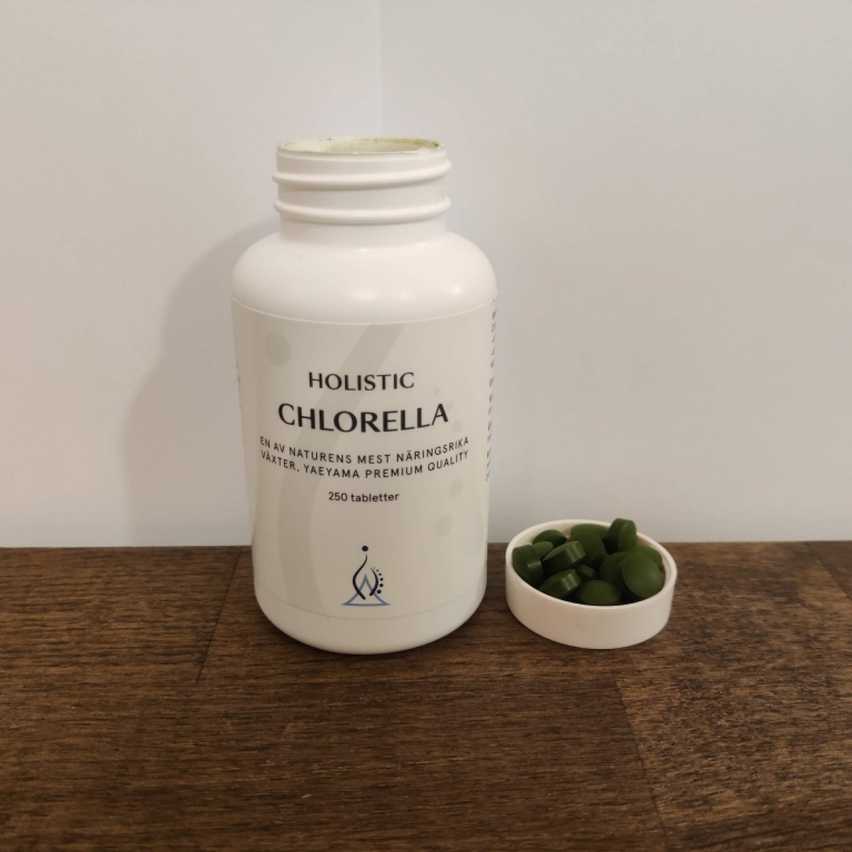 Holistic Chlorella öppnad burk med gröna tabletter på träbord taget av oss under testet