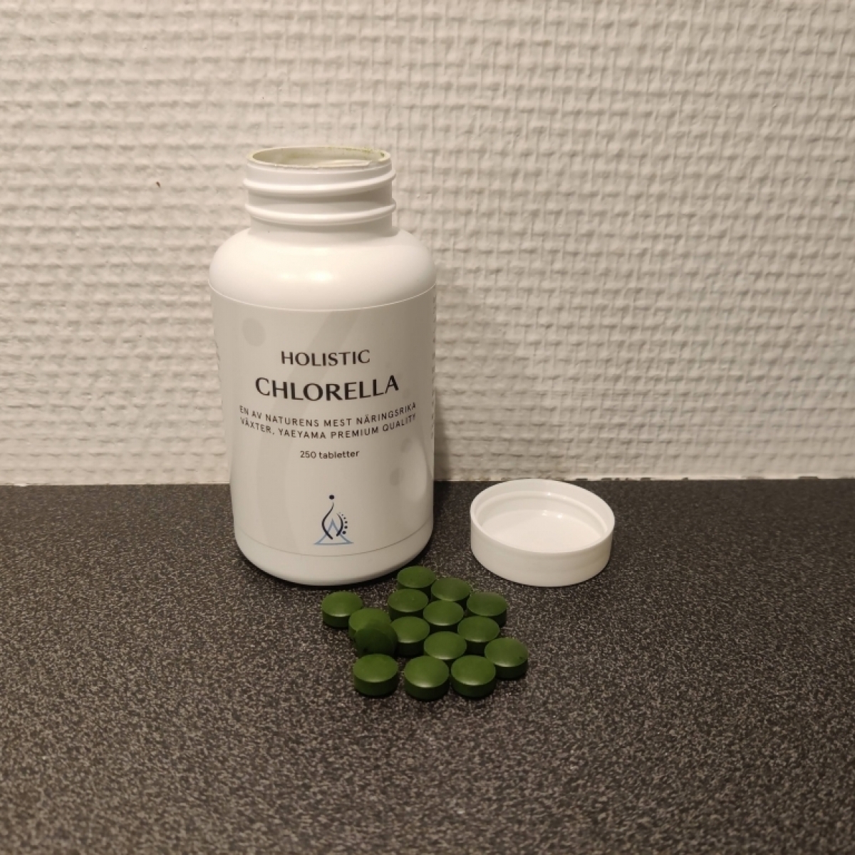 Holistic Chlorella öppnad burk med utspridda tabletter på mörk bänk taget av oss