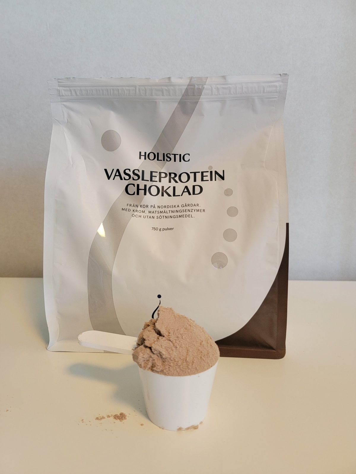 Holistic Vassleprotein choklad fotograferad av oss under testet, med skopa fylld av luftigt pulver