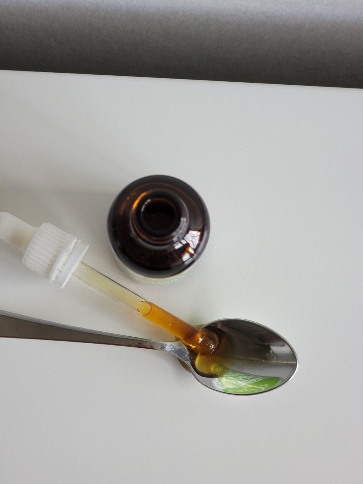 Närbild uppifrån av Healthwell Vitamin E Komplex där en seg droppe samlas i skeden under dosering