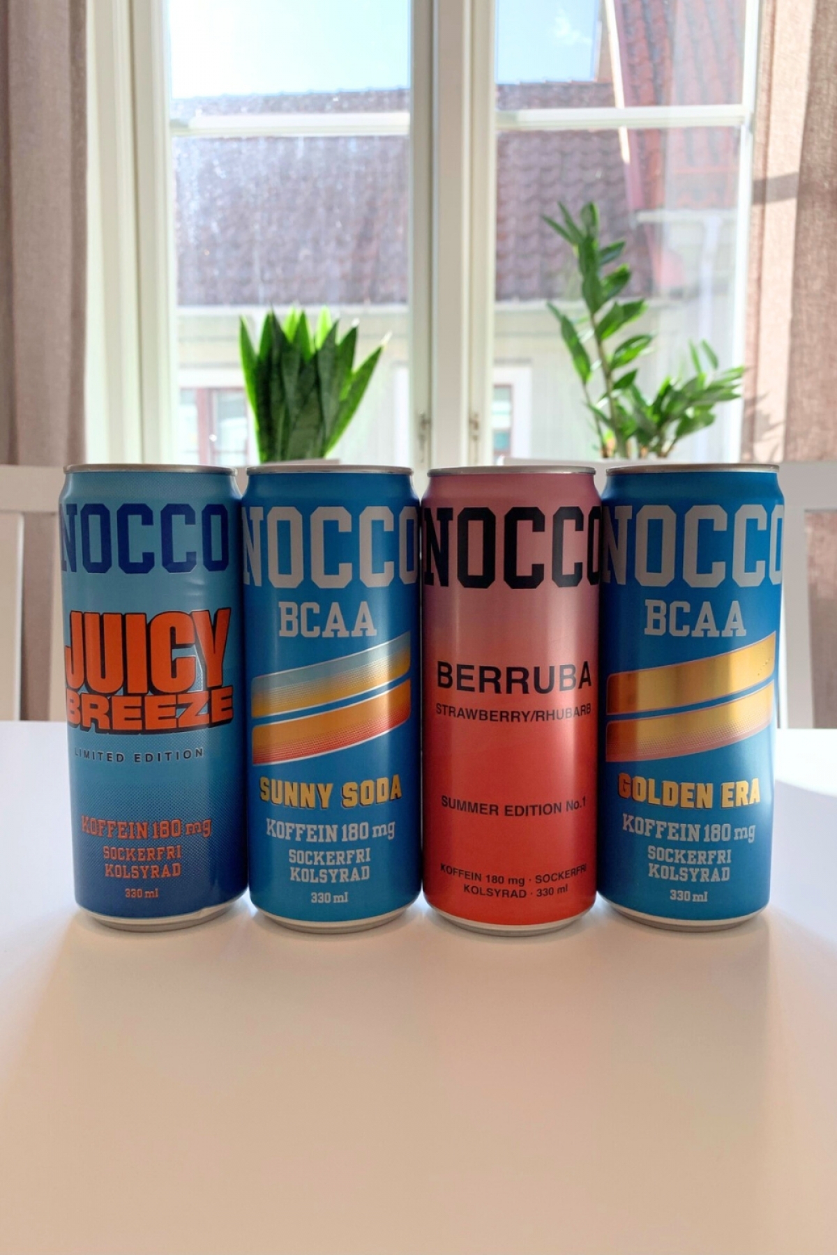 Fyra NOCCO BCAA-burkar i fönsterljus under vårt test Juicy Breeze Sunny Soda Berruba och Golden Era fotade av oss