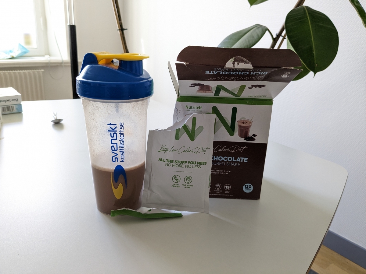 Färdigblandad Nutrilett chokladshake i shaker bredvid öppnad kartong tagen av oss
