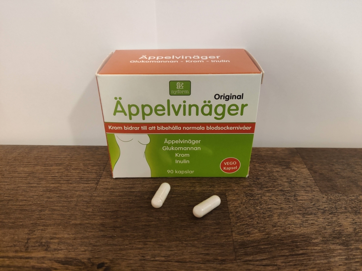 Två kapslar framför förpackningen Nyform Äppelvinäger Krom fotograferat av oss