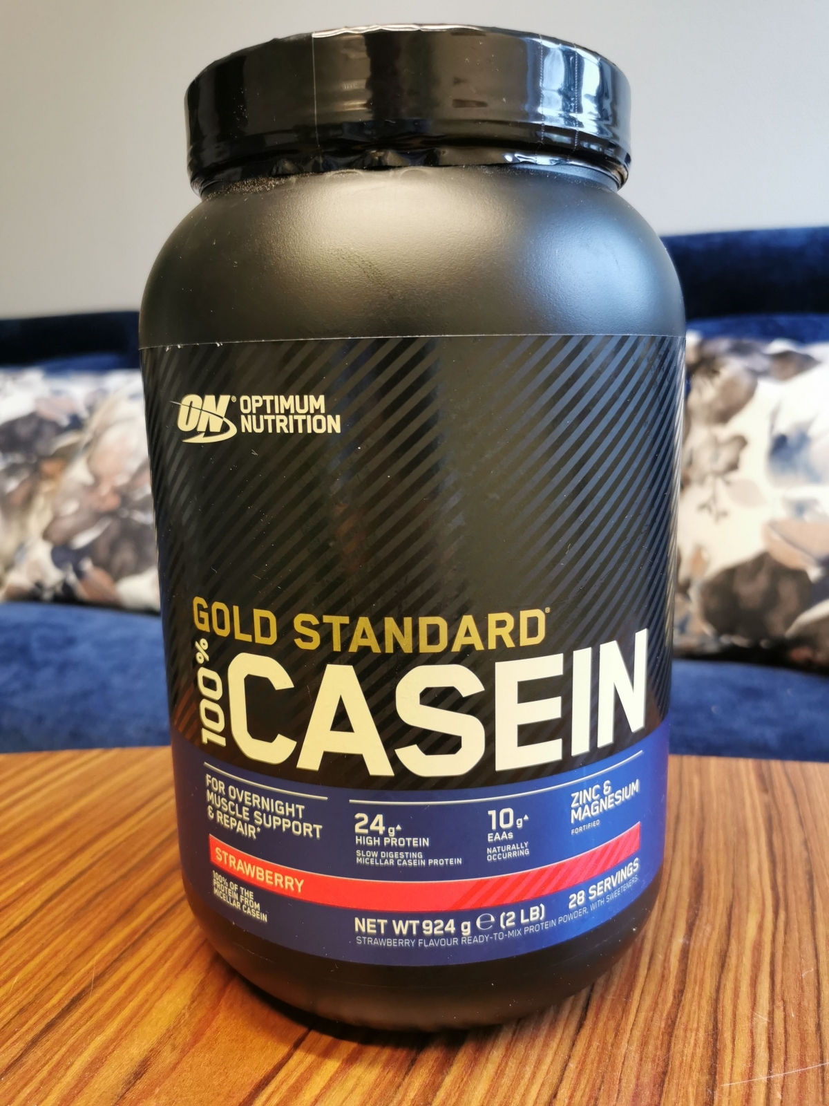 Vår egen bild på Optimum Nutrition Gold Standard 100% Casein, framsida av burk på bord och tydliga näringspunkter
